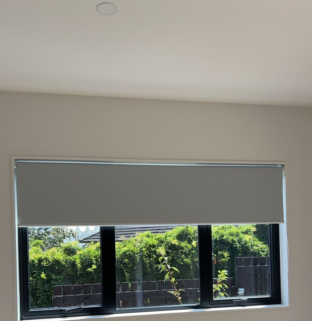 Grey roller blind with garden hedge view